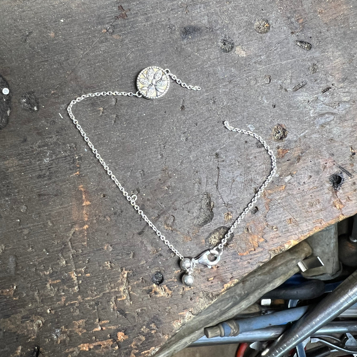 Silver necklace on a worn metal surface with tools in the background