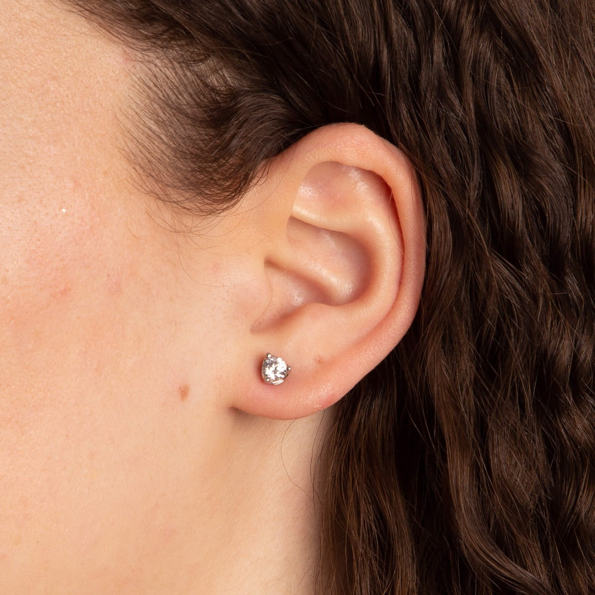 Close-up of an ear wearing a diamond stud earring with hair partially covering the frame.