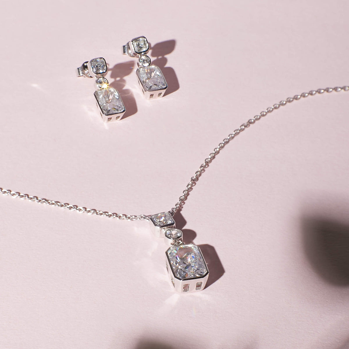 Silver necklace and earrings with gemstones on a pink background