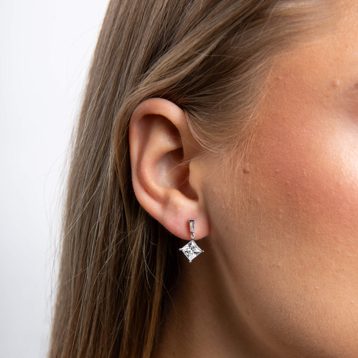 Close-up of an ear wearing a diamond earring with a plain background