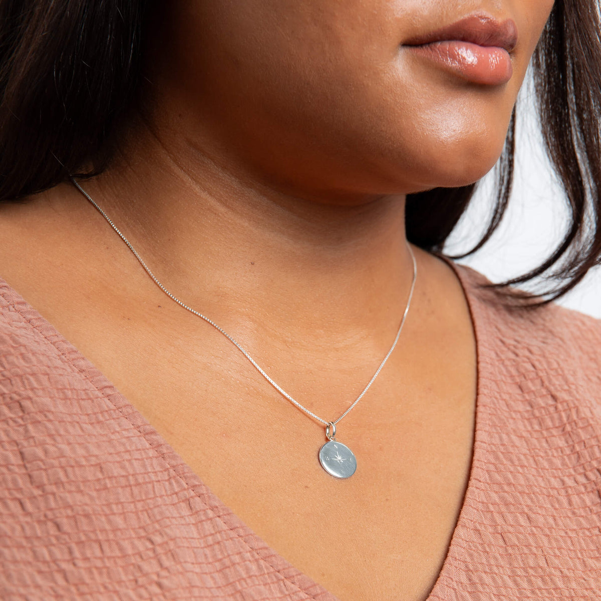 Close-up of a person wearing a silver necklace with a pendant.