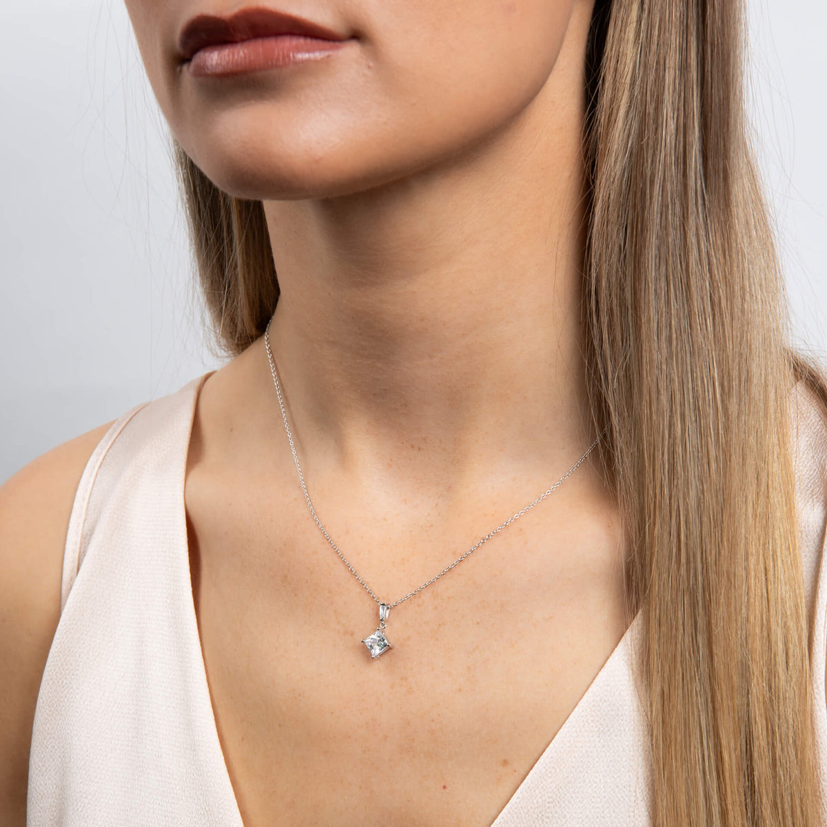 Woman wearing a delicate necklace with a small pendant against a neutral background