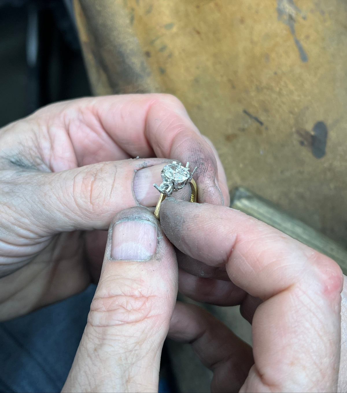 Close-up of hands holding a gold ring with a diamond on a wooden surface.