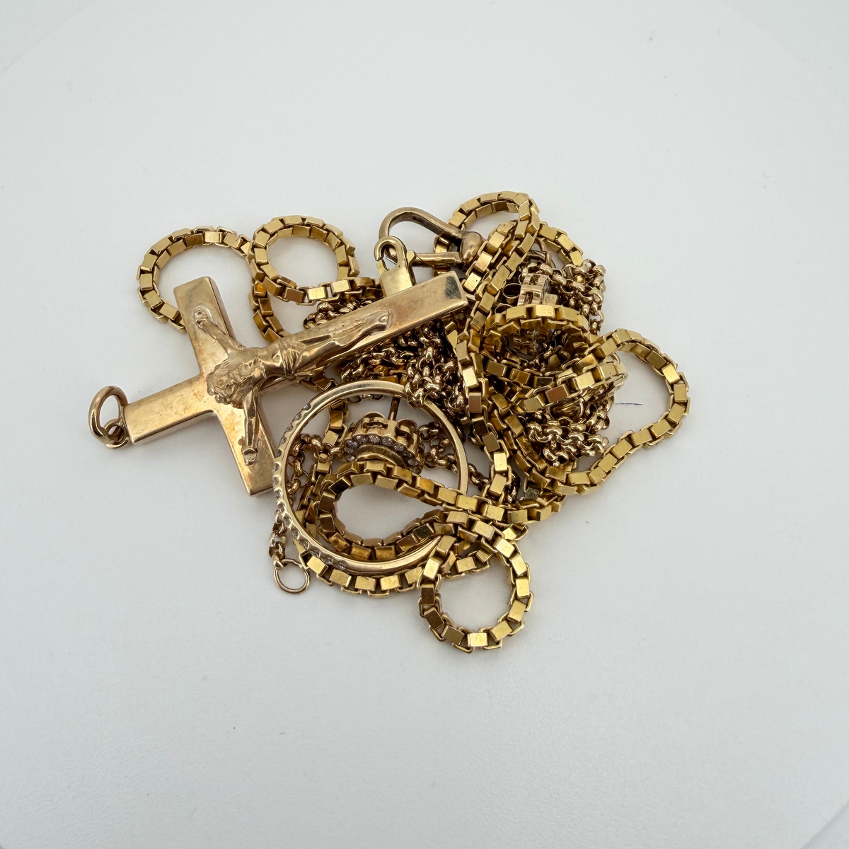 A pile of gold-toned chain necklaces and jewelry pieces with a cross pendant, arranged on a white circular plate against a light gray background.