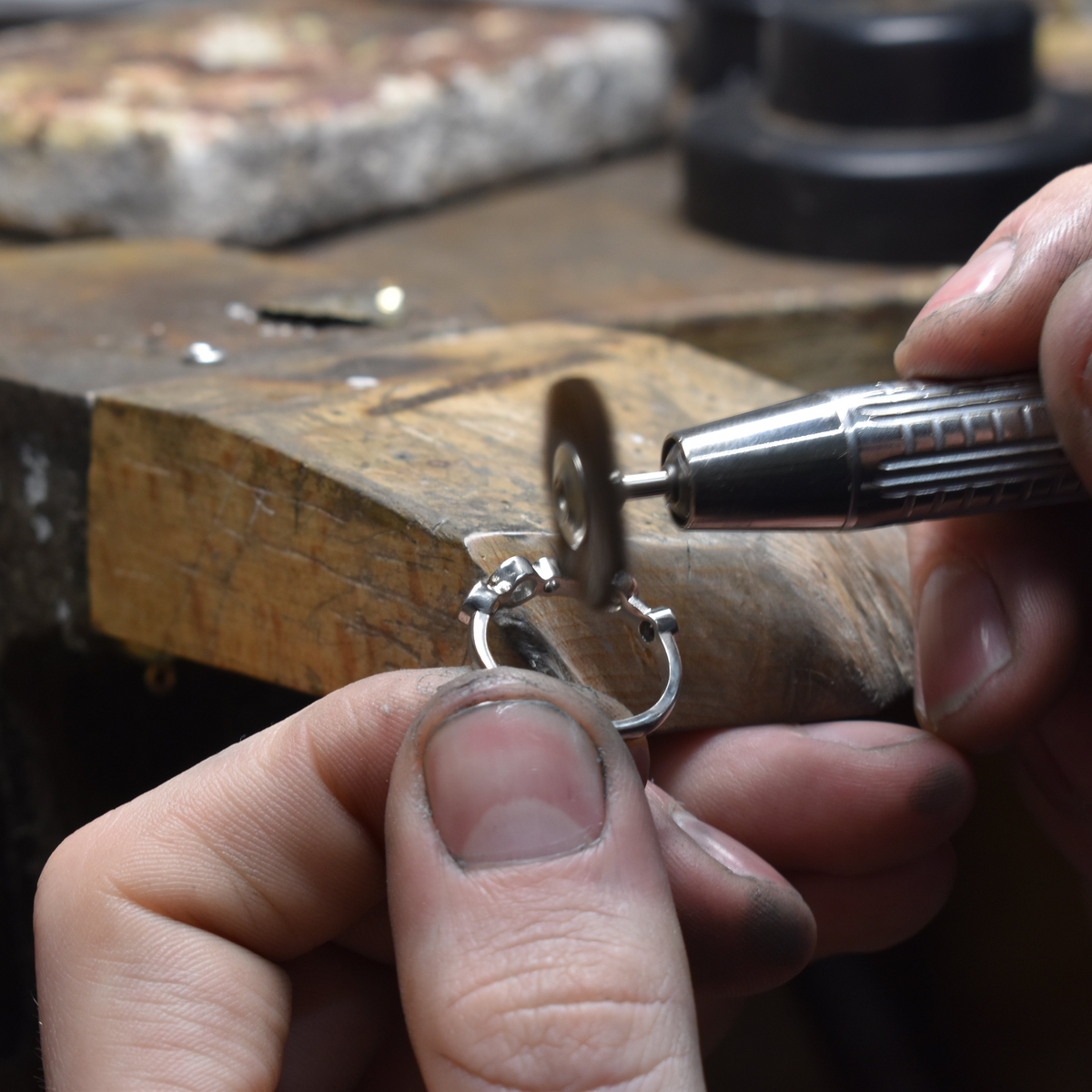 Person working on a piece of jewelry with a tool on a wooden surface