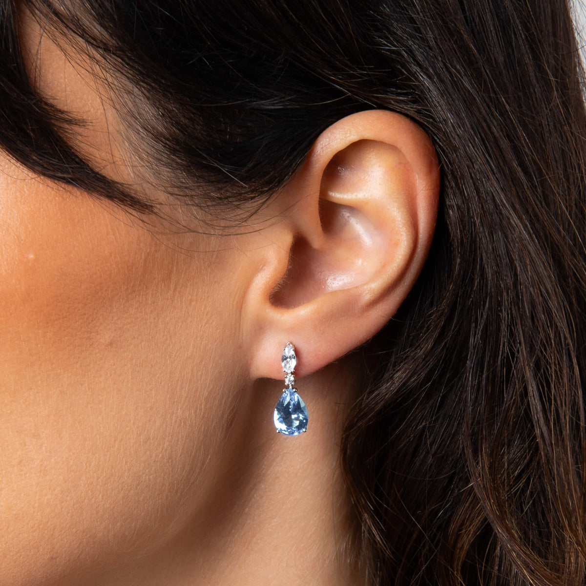 Close-up of an ear wearing a blue teardrop earring with dark hair.