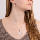 Close-up of a woman wearing a diamond necklace and earrings on a plain background