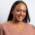 Woman wearing a pink top and a necklace with a heart pendant against a white background