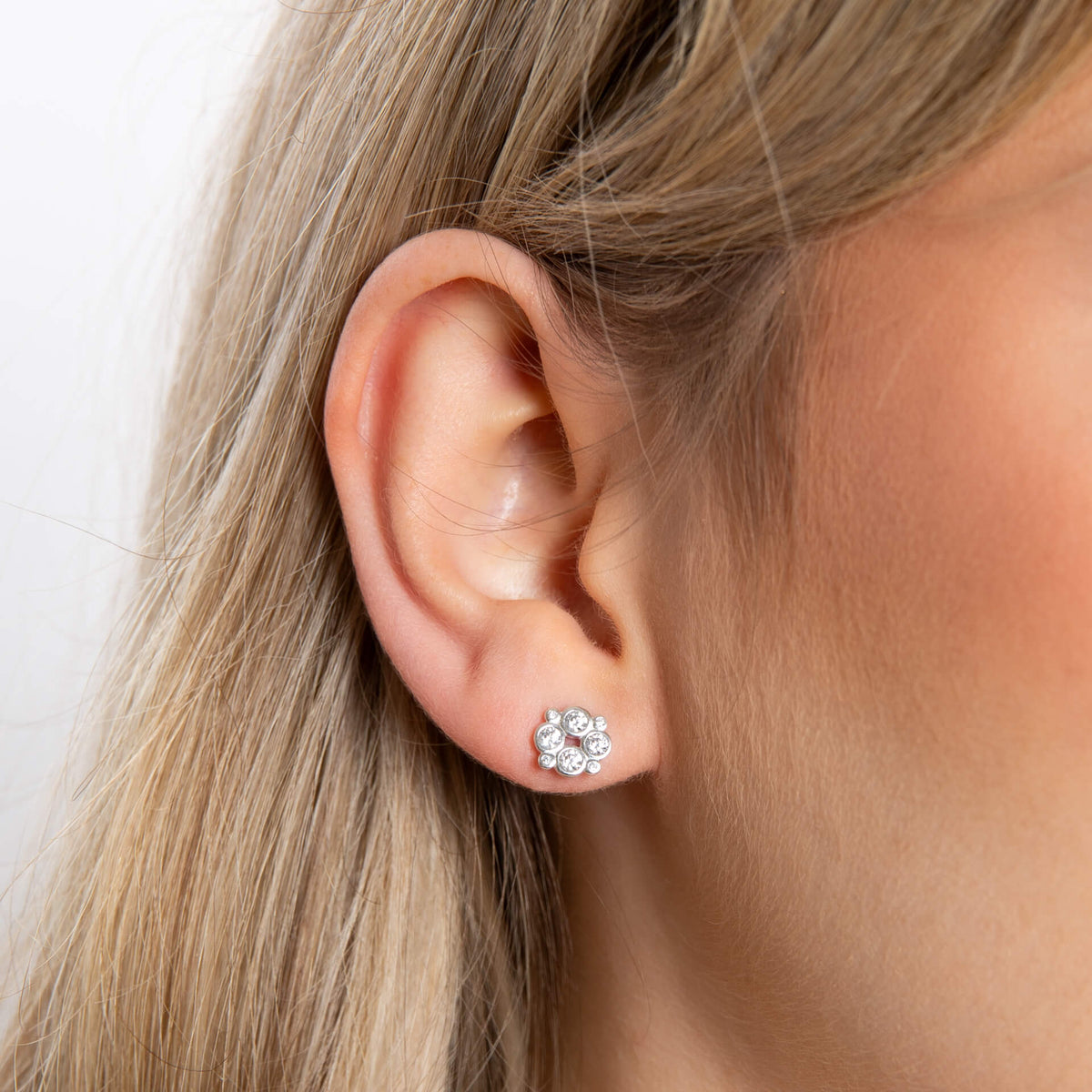 Close-up of an ear wearing a diamond stud earring with a blurred background