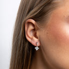 Close-up of an ear wearing a diamond earring with a plain background