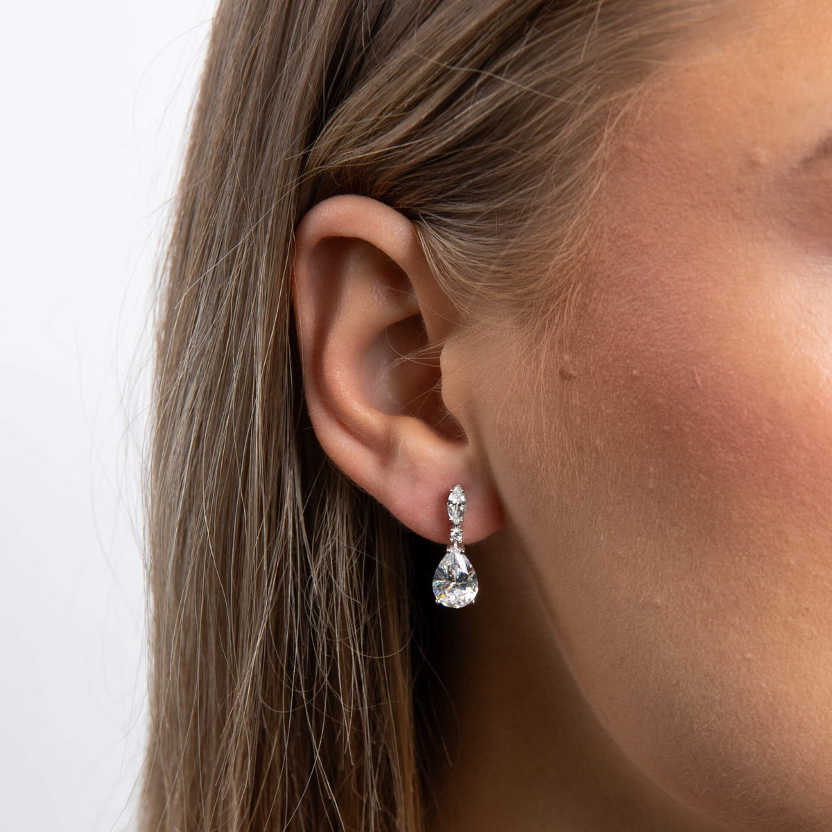 Close-up of a woman wearing a teardrop-shaped earring with a plain background