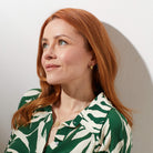 Woman with red hair wearing a green and white patterned shirt against a plain background