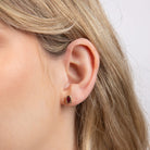 Close-up of an ear wearing a small red gemstone earring with blonde hair.