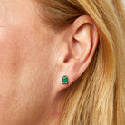 Close-up of an ear wearing a green gemstone earring with blonde hair.