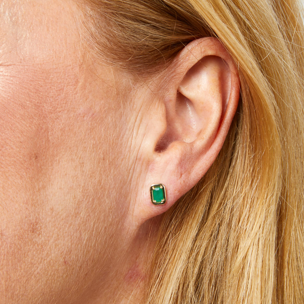 Close-up of an ear wearing a green gemstone earring with blonde hair.