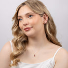 Woman wearing a delicate necklace with a small red pendant against a plain background