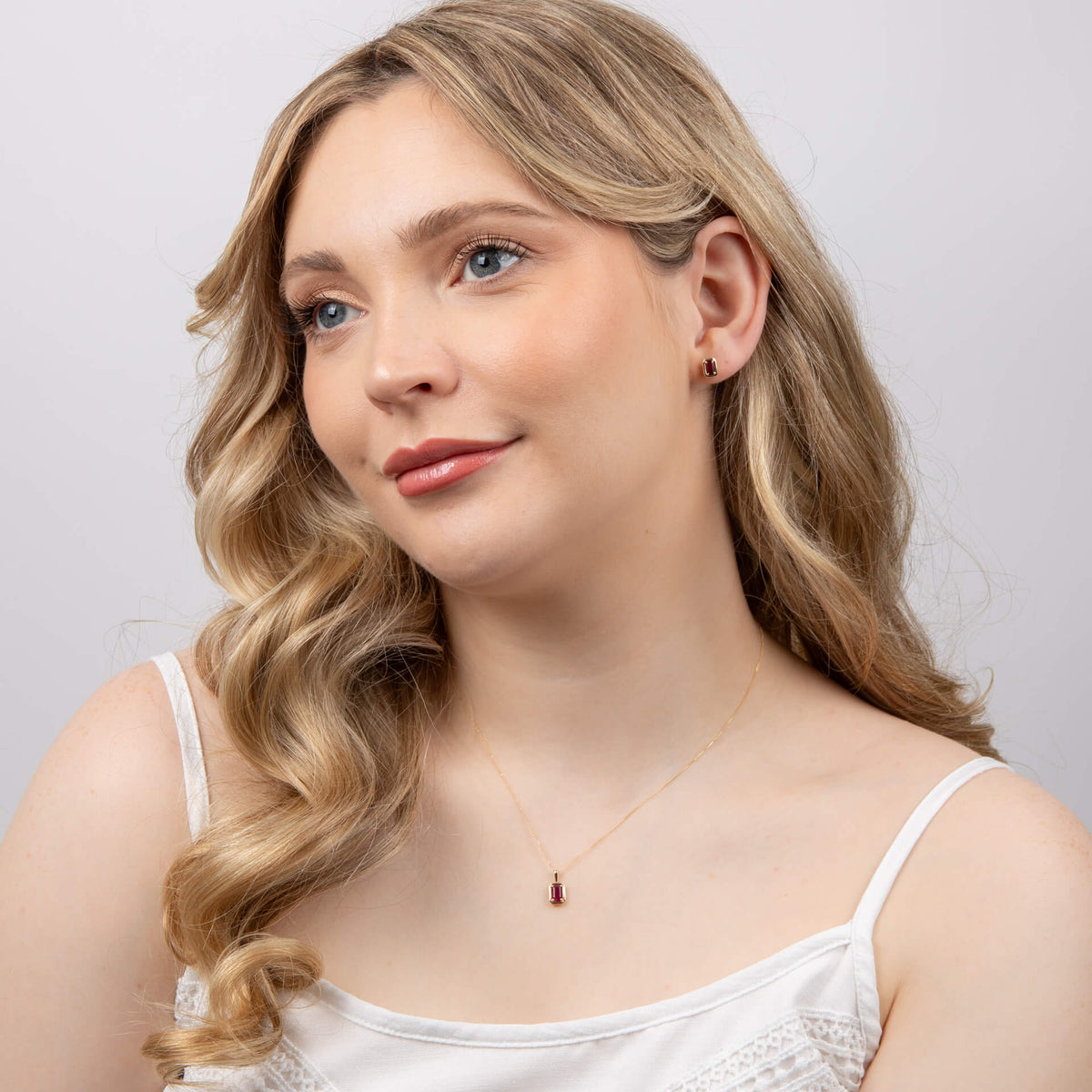 Woman wearing a delicate necklace with a small red pendant against a plain background