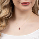 Close-up of a person wearing a gold necklace with a red gemstone pendant.