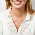 Woman wearing a gold necklace with a green gemstone pendant on a white background