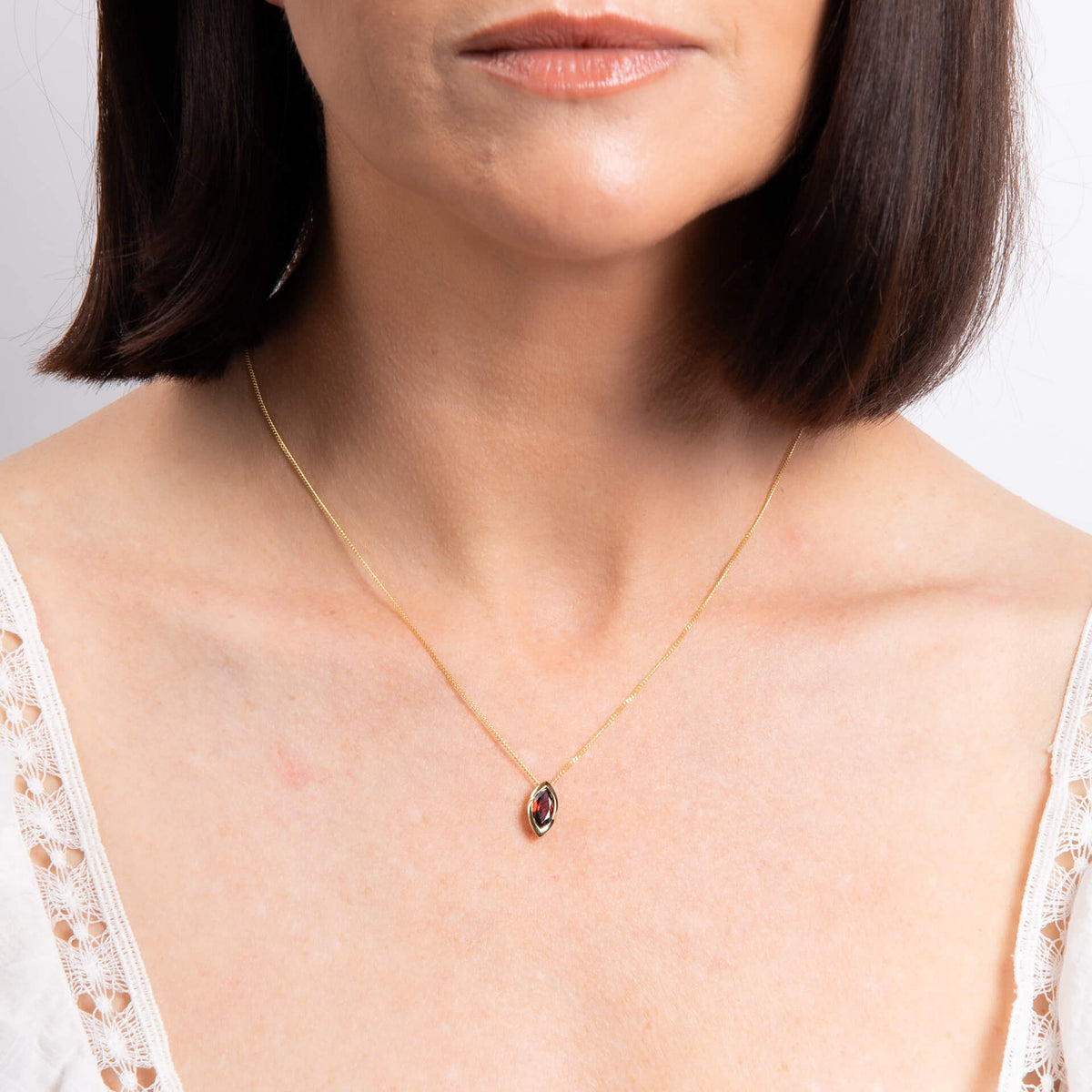 Woman wearing a delicate gold necklace with a small pendant on a plain background