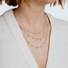 Close-up of a person wearing multiple necklaces with a neutral background