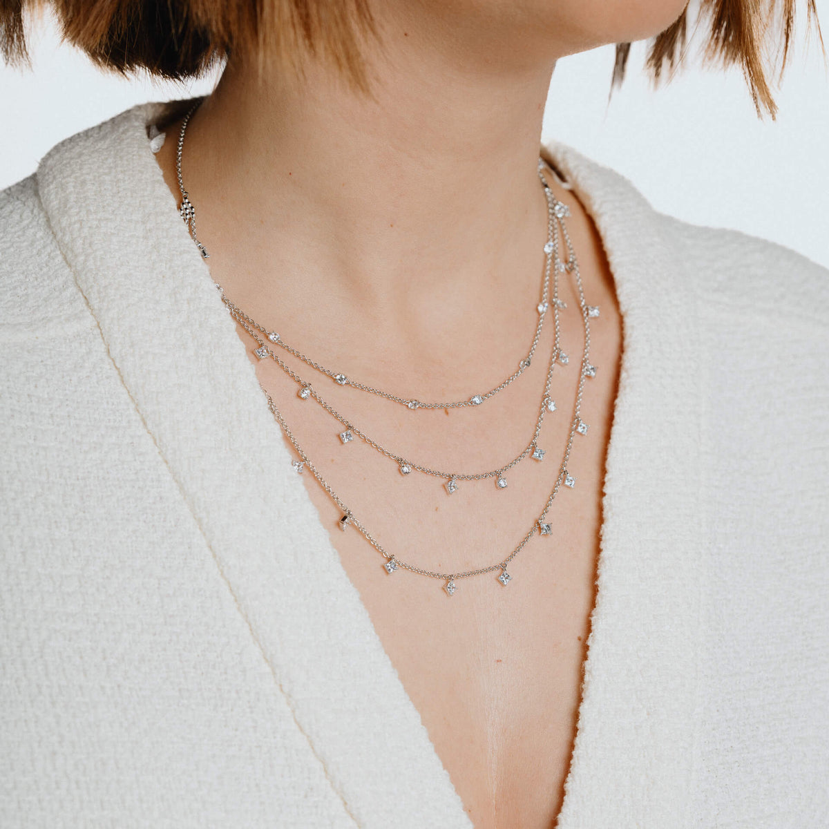 Close-up of a person wearing multiple necklaces with a neutral background