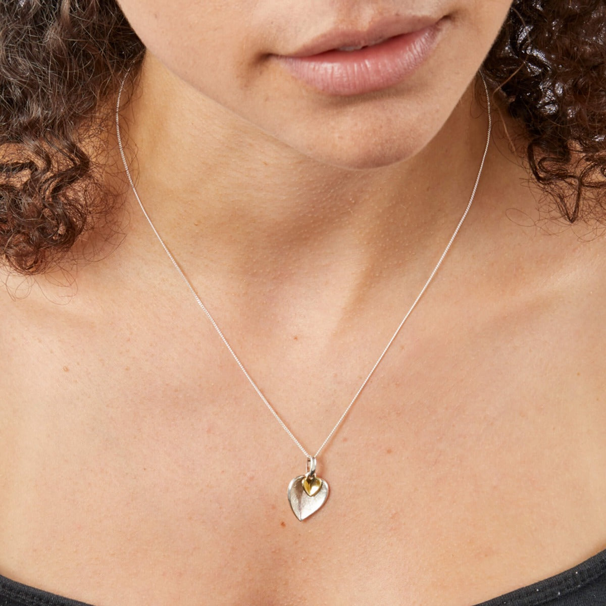 Close-up of a person wearing a silver necklace with a heart-shaped pendant.