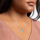 Close-up of a person wearing a silver necklace with a pendant.