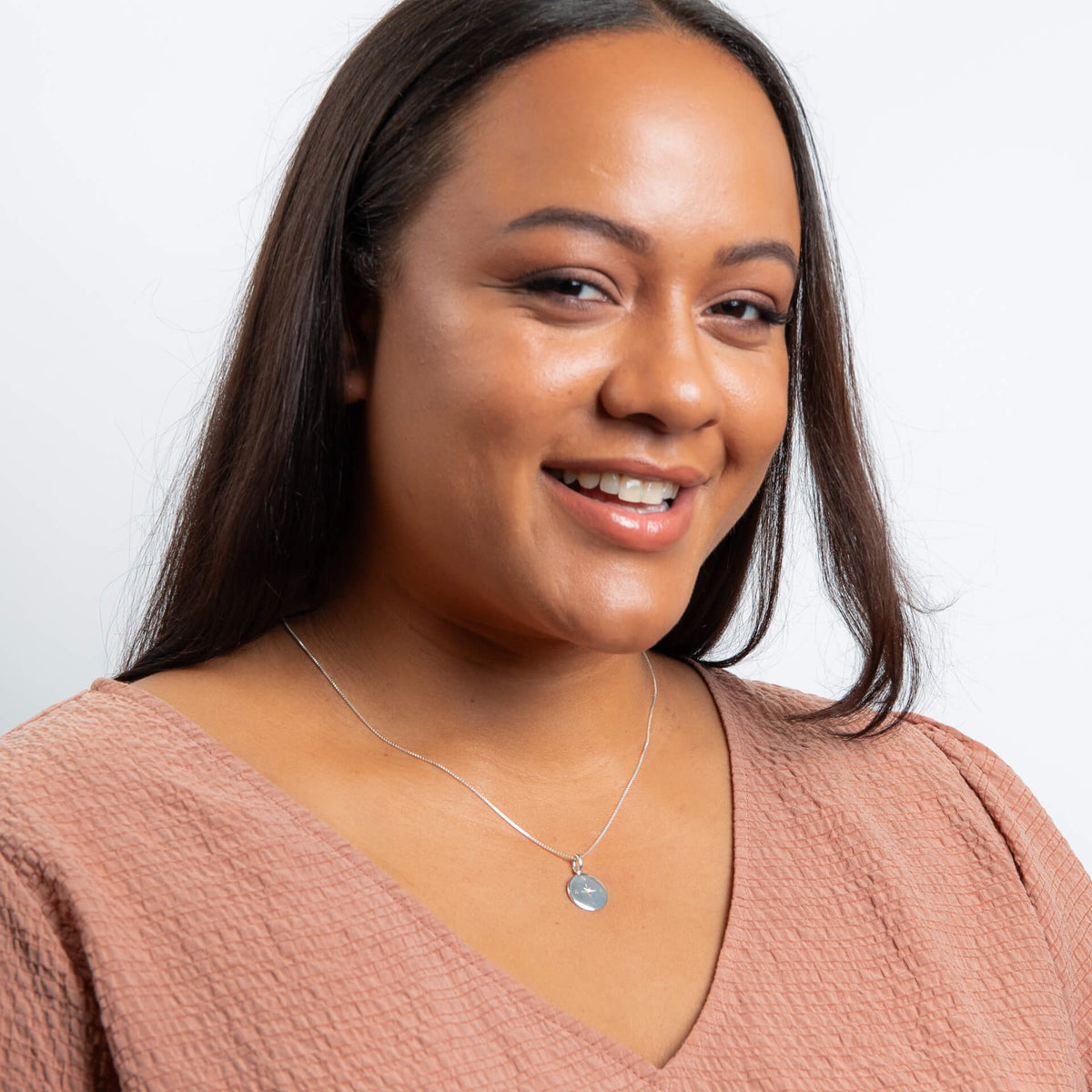 Woman wearing a pink top and necklace with a white background