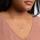 Silver necklace with a clover pendant worn by a person in a pink top.