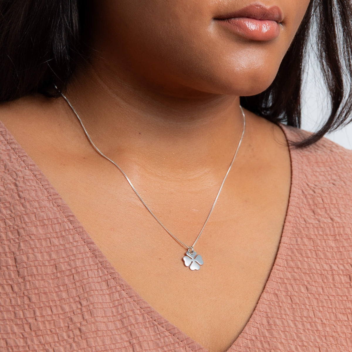 Silver necklace with a clover pendant worn by a person in a pink top.