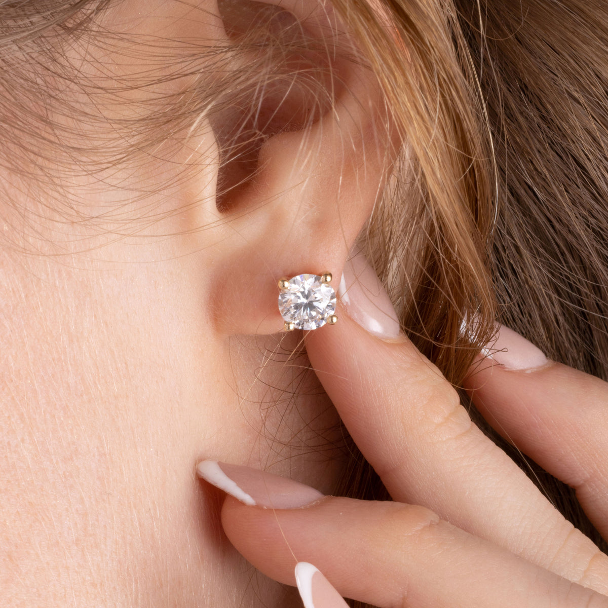 Close-up of a diamond earring being worn, with a hand adjusting it.
