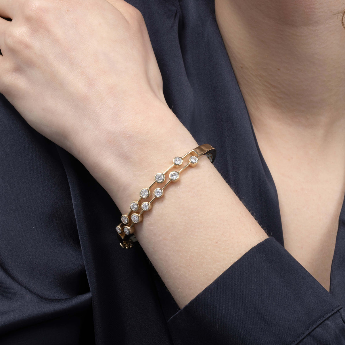 Gold bracelet with diamonds on a person's wrist against a dark background